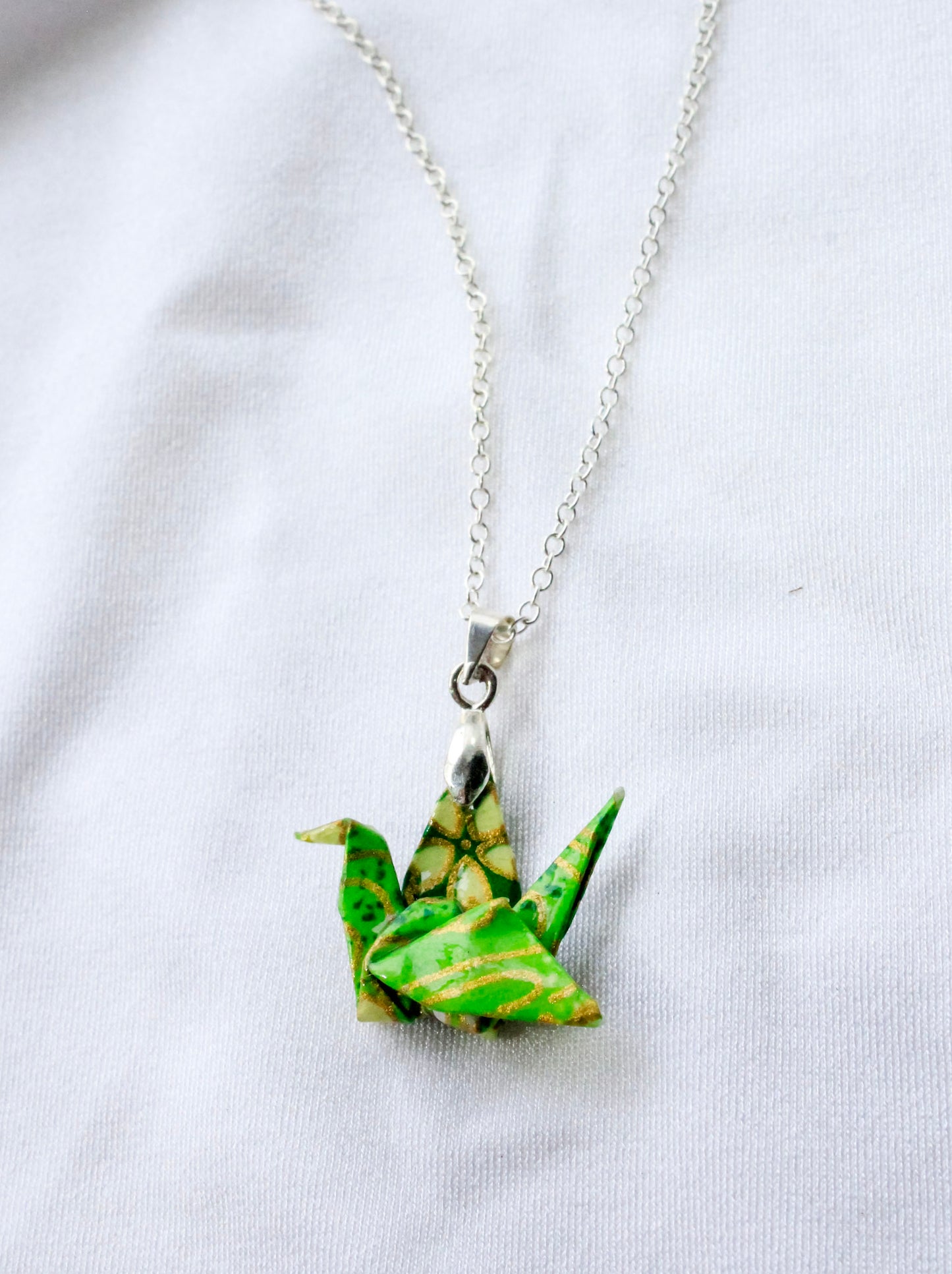 Handmade origami crane necklace with blue wave patterns on a silver chain, displayed on a white background.