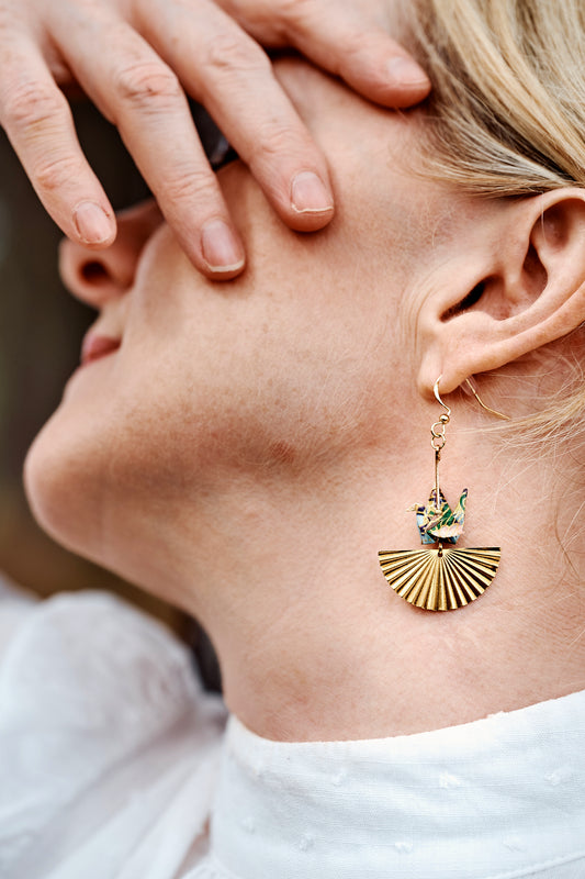 Close-up of a person wearing a gold earring with a green gemstone.