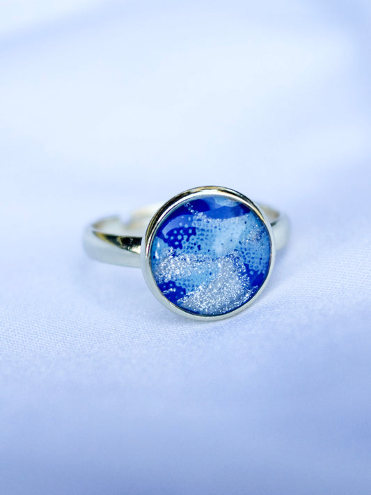 Silver ring with a blue circular gemstone on a light purple background