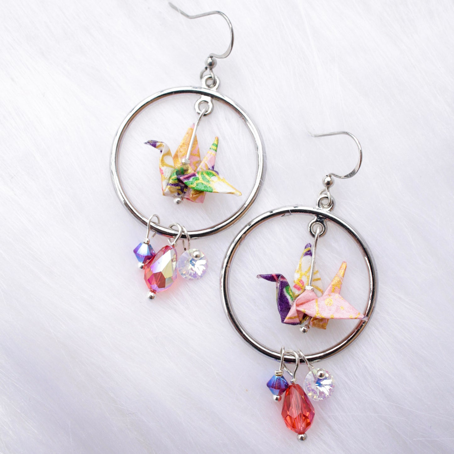 A pair of origami crane earrings with blue and multicolored accents, adorned with sparkling Swarovski crystals, suspended from silver hooks.