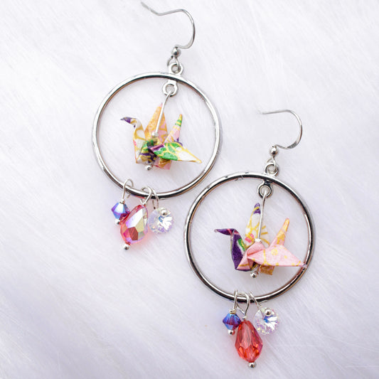 A pair of origami crane earrings with blue and multicolored accents, adorned with sparkling Swarovski crystals, suspended from silver hooks.