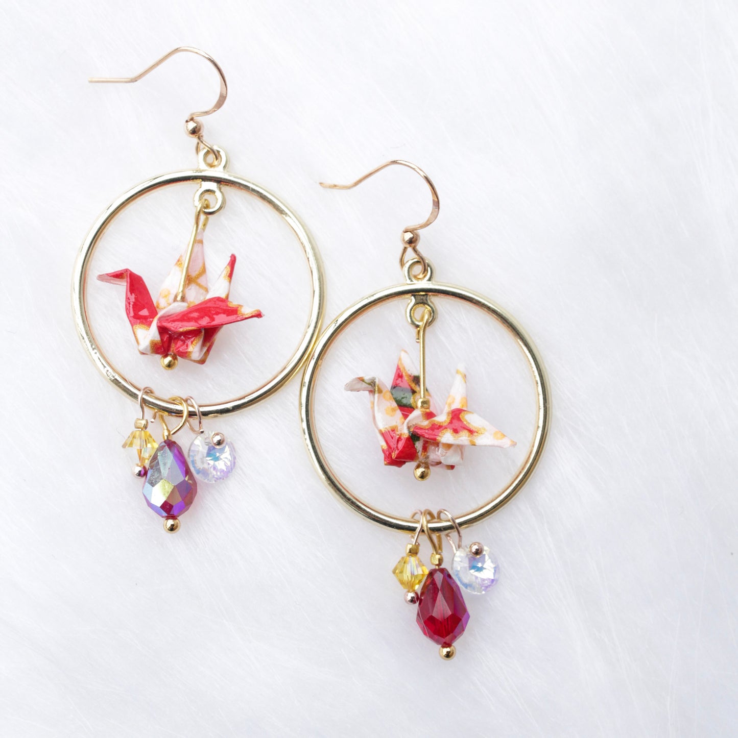 A pair of origami crane earrings with blue and multicolored accents, adorned with sparkling Swarovski crystals, suspended from silver hooks.