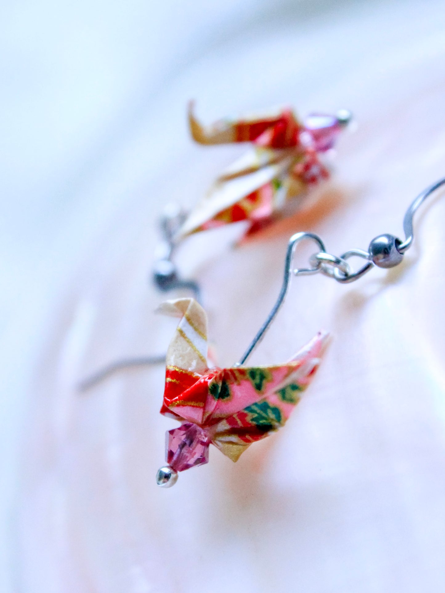 A hand-folded origami crane earrings in blue and white, perched atop a Swarovski crystal, with gold-colored hooks.