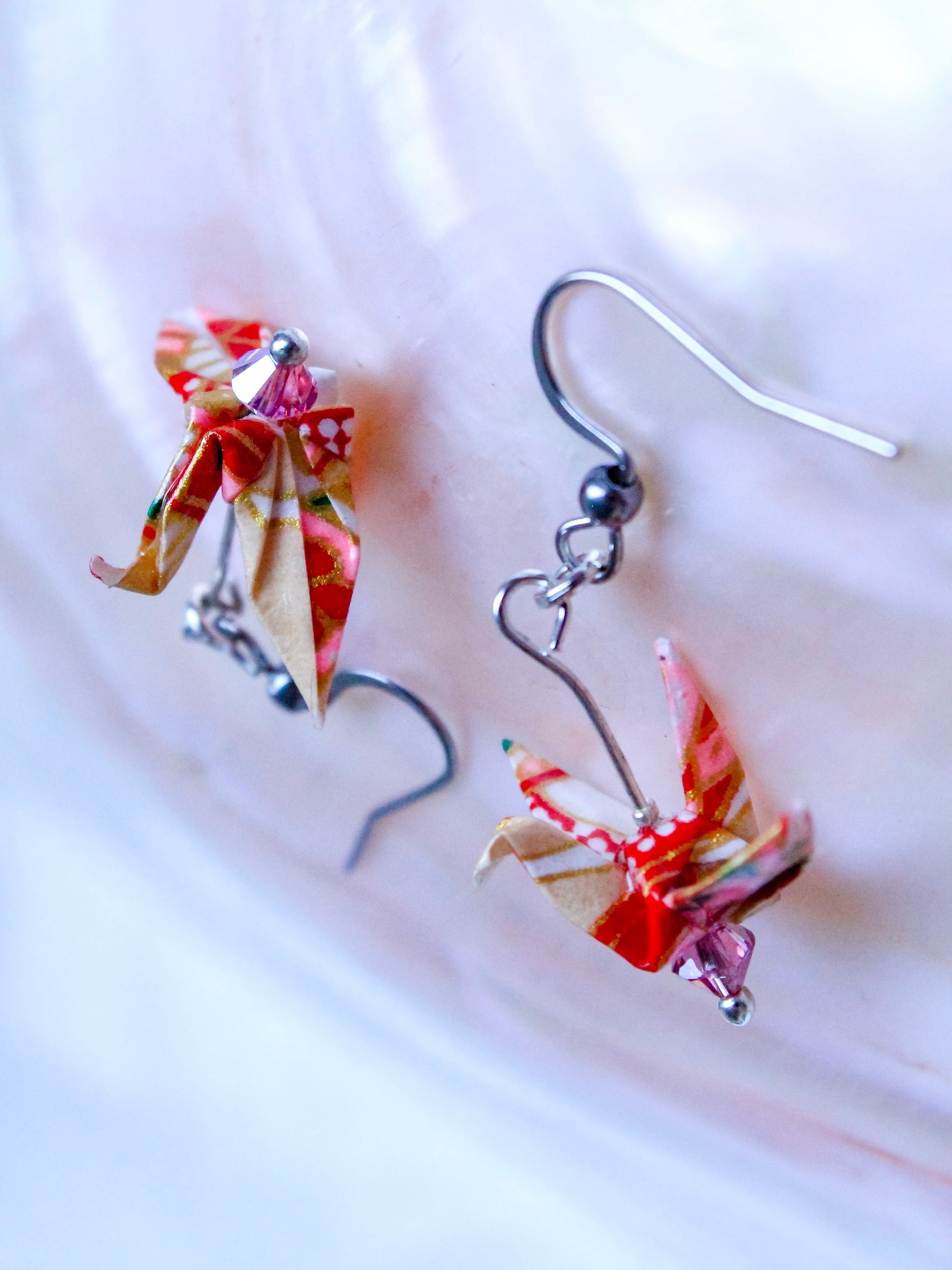 A hand-folded origami crane earrings in blue and white, perched atop a Swarovski crystal, with gold-colored hooks.