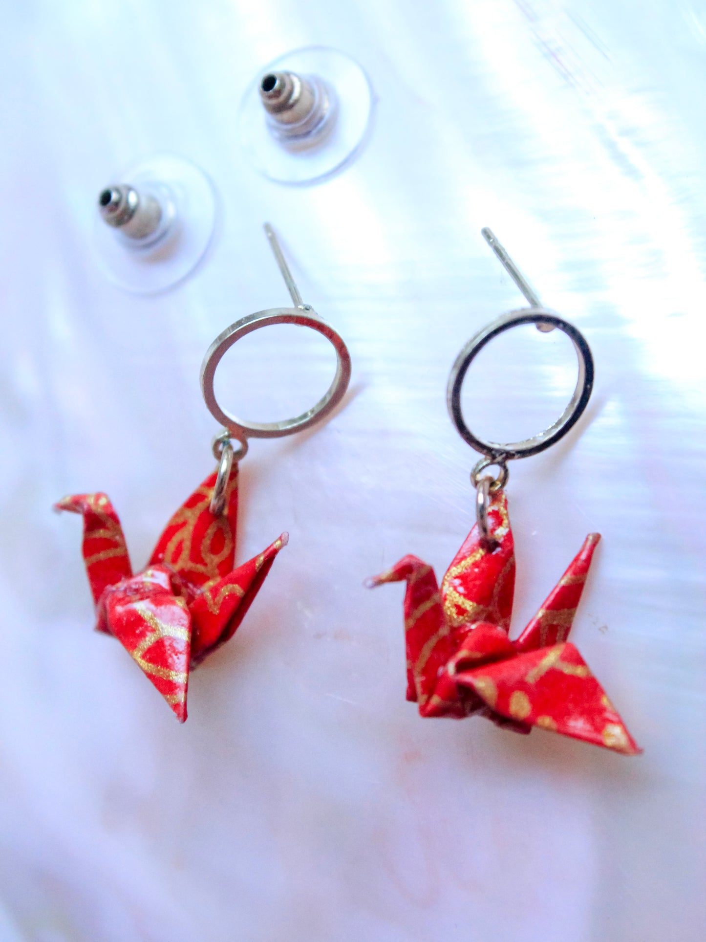A pair of origami crane hoop earrings with red and gold color patterns, displayed against a white background.