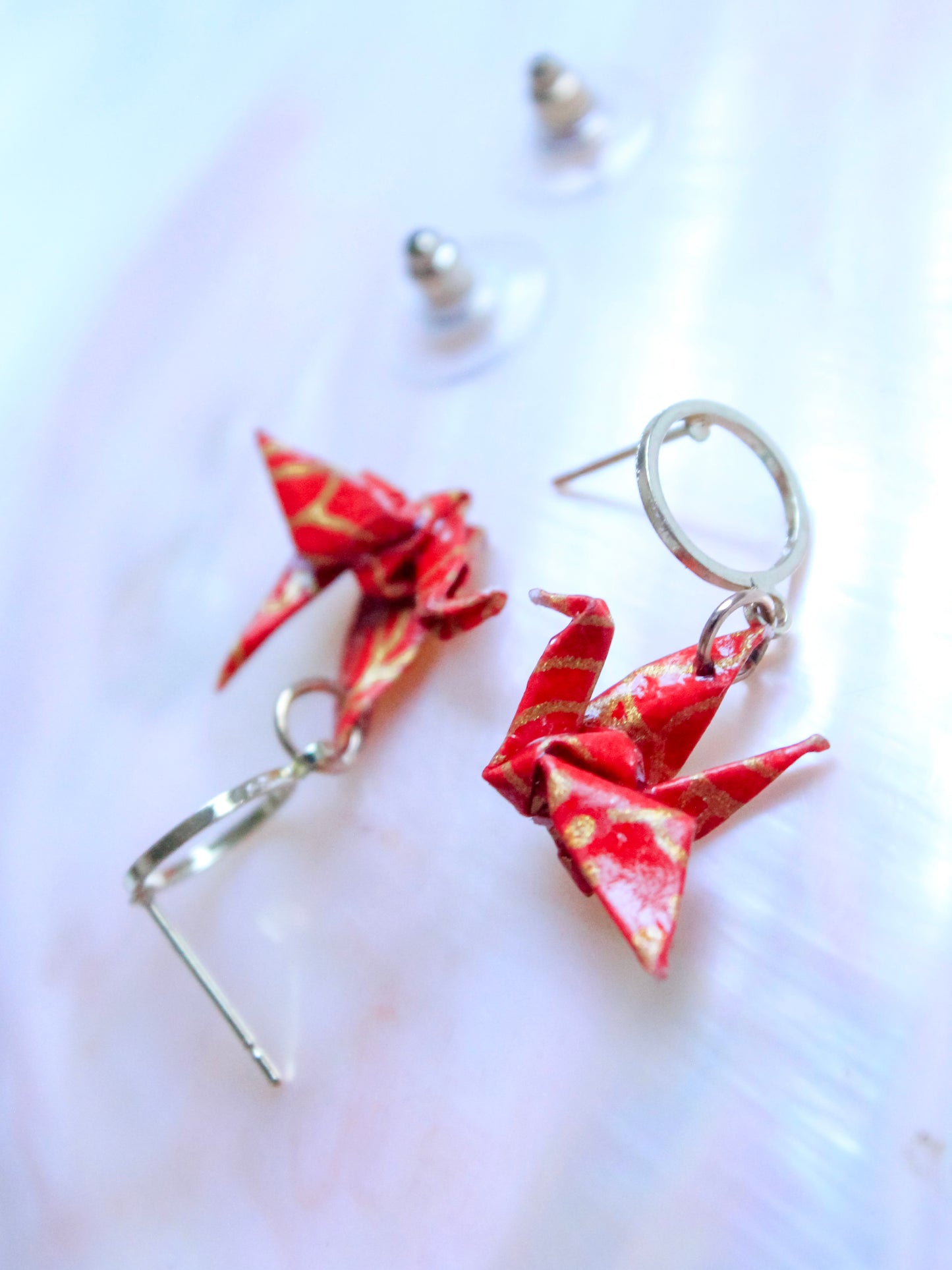 A pair of origami crane hoop earrings with multicolored patterns, displayed against a pink background.