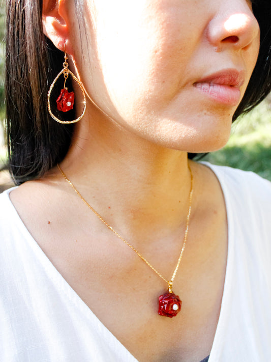 Close-up of a person wearing a gold necklace with a red pendant.
